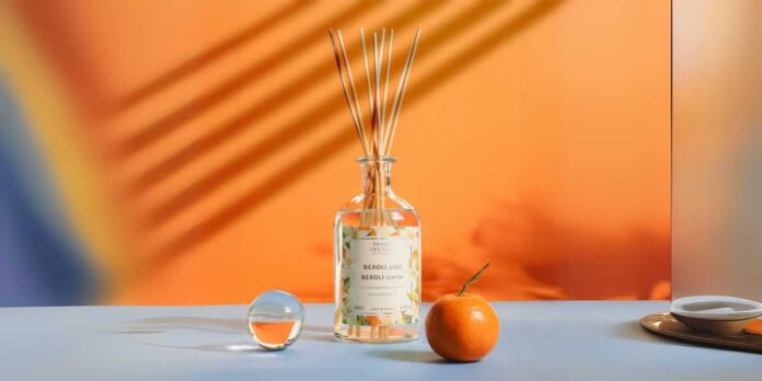 Difusores de Aromas para Casa, em um fundo laranja, varetas de bambú, uma esfera de cristal, e uma fruta laranja